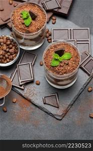 Classic tiramisu dessert in a glass and pieces of chocolate on dark concrete background or table. Classic tiramisu dessert in a glass and pieces of chocolate on dark concrete background