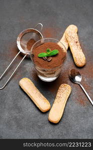 Classic tiramisu dessert in a glass and savoiardi cookie on dark concrete background or table. Classic tiramisu dessert in a glass and savoiardi cookies on dark concrete background