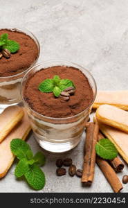 Classic tiramisu dessert in a glass and savoiardi cookies on concrete background or table. Classic tiramisu dessert in a glass and savoiardi cookies on concrete background