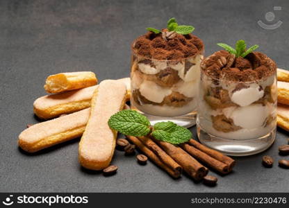 Classic tiramisu dessert in a glass and savoiardi cookies on dark concrete background or table. Classic tiramisu dessert in a glass and savoiardi cookies on dark concrete background