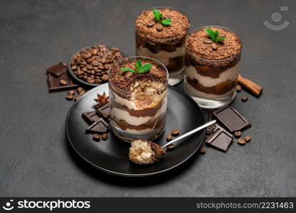 Classic tiramisu dessert in a glass cup and pieces of chocolate on dark concrete background or table. Classic tiramisu dessert in a glass cup and pieces of chocolate on dark concrete background