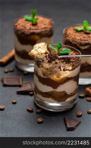 Classic tiramisu dessert in a glass cup and pieces of chocolate on dark concrete background or table. Classic tiramisu dessert in a glass cup and pieces of chocolate on dark concrete background