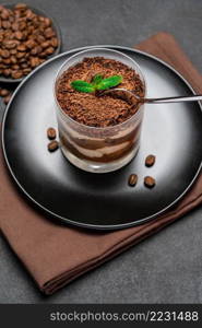 Classic tiramisu dessert in a glass cup and pieces of chocolate on dark concrete background or table. Classic tiramisu dessert in a glass cup and pieces of chocolate on dark concrete background