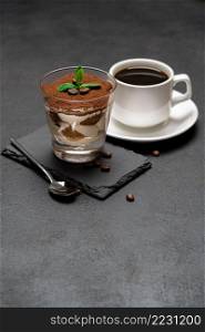 Classic tiramisu dessert in a glass on stone serving board and cup of coffee on dark concrete background or table. Classic tiramisu dessert in a glass on stone serving board and cup of coffee on dark concrete background
