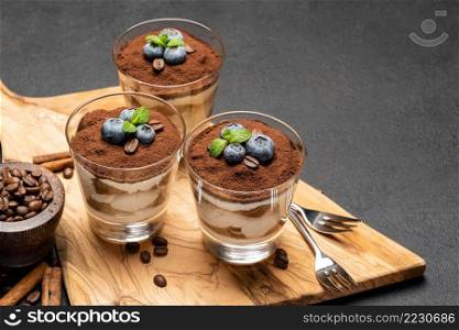 Classic tiramisu dessert in a glass with blueberries on dark concrete background or table. Classic tiramisu dessert in a glass with blueberries on dark concrete background