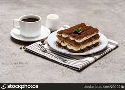 Classic tiramisu dessert on ceramic plate and cup of coffee on concrete background or table. Classic tiramisu dessert on ceramic plate, milk or cream and cup of coffee on concrete background