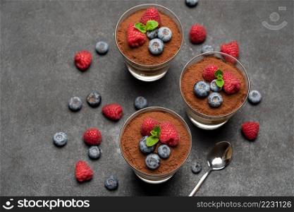 Classic tiramisu dessert with blueberries and raspberries in a glass on dark concrete background or table. Classic tiramisu dessert with blueberries and raspberries in a glass on dark concrete background