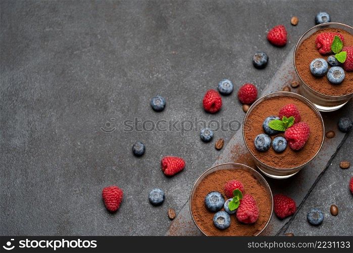 Classic tiramisu dessert with blueberries and raspberries in a glass on stone serving board on dark concrete background or table. Classic tiramisu dessert with blueberries and raspberries in a glass on stone serving board on dark concrete background