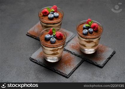 Classic tiramisu dessert with blueberries and raspberries in a glass on stone serving board on dark concrete background or table. Classic tiramisu dessert with blueberries and raspberries in a glass on stone serving board on dark concrete background