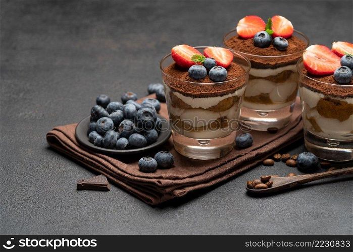 Classic tiramisu dessert with blueberries and strawberries in a glass on dark concrete background or table. Classic tiramisu dessert with blueberries and strawberries in a glass on dark concrete background