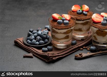 Classic tiramisu dessert with blueberries and strawberries in a glass on dark concrete background or table. Classic tiramisu dessert with blueberries and strawberries in a glass on dark concrete background