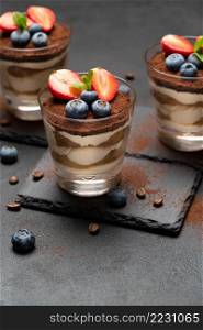 Classic tiramisu dessert with blueberries and strawberries in a glass on stone serving board on dark concrete background or table. Classic tiramisu dessert with blueberries and strawberries in a glass on stone serving board on dark concrete background