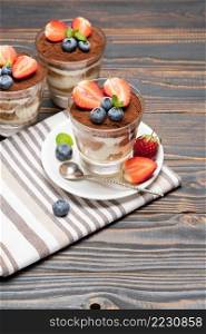Classic tiramisu dessert with blueberries and strawberries in a glass on wooden background or tab≤. Classic tiramisu dessert with blueberries and strawberries in a glass on wooden background