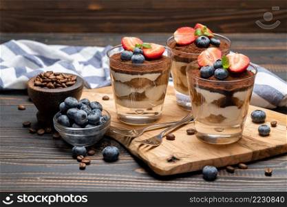 Classic tiramisu dessert with blueberries and strawberries in a glass on wooden background or table. Classic tiramisu dessert with blueberries and strawberries in a glass on wooden background