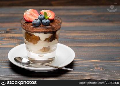 Classic tiramisu dessert with blueberries and strawberries in a glass on wooden background or table. Classic tiramisu dessert with blueberries and strawberries in a glass on wooden background