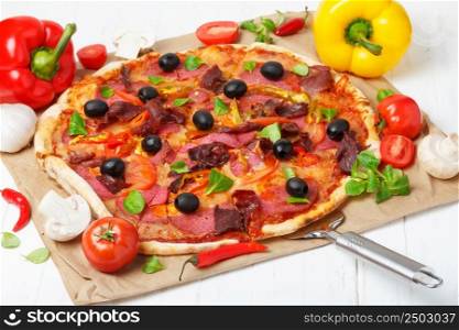 Classic traditional home made pizza with ham and salami on white kitchen wooden table