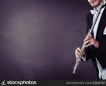 Classical music, passion and hobby concept. Elegantly dressed musician man holding flute. Studio shot on dark background. Elegantly dressed musician holding flute