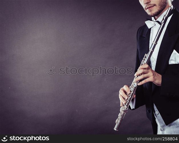 Classical music, passion and hobby concept. Elegantly dressed musician man holding flute. Studio shot on dark background. Elegantly dressed musician holding flute