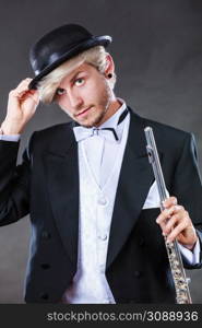 Classical music, passion and hobby concept. Elegantly dressed musician man holding flute wearing black hat. Studio shot on dark background. Elegantly dressed musician holding flute