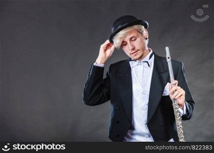 Classical music, passion and hobby concept. Elegantly dressed musician man holding flute wearing black hat. Studio shot on dark background. Elegantly dressed musician holding flute