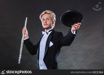 Classical music, passion and hobby concept. Elegantly dressed musician man holding flute wearing black hat. Studio shot on dark background. Elegantly dressed musician holding flute