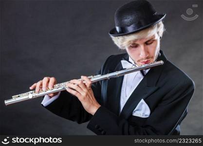 Classical music, passion and hobby concept. Elegantly dressed musician man playing on flute wearing black fedora hat. Studio shot on dark grey background. Elegantly dressed male musician playing flute