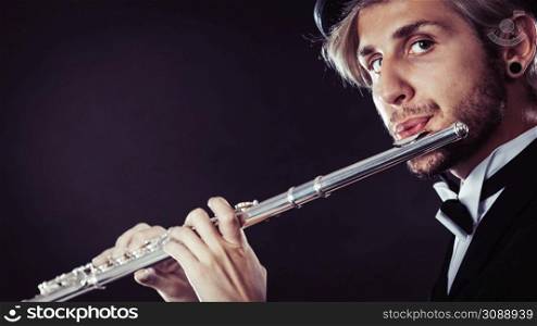 Classical music, passion and hobby concept. Elegantly dressed musician man playing on flute wearing black fedora hat. Studio shot on dark grey background. Elegantly dressed male musician playing flute