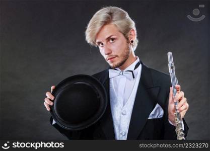 Classical music, passion, hobby concept. Elegantly dressed musician man holding flute and black fedora hat. Studio shot on dark background. Elegantly dressed musician holding flute