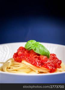 Classical spaghetti with tomato sauce on blue background with basil