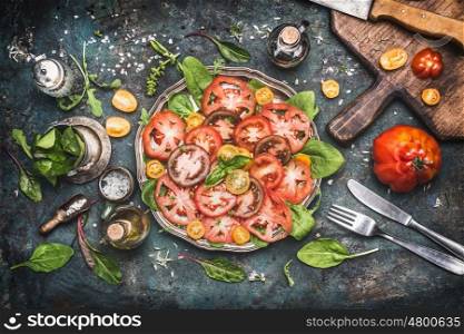 Classical traditional tomatoes mozzarella salad , preparation on dark rustic kitchen table with ingredients , cutting board and cutlery , top view