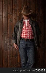 classically dressed middle-aged cowboy in wide-brimmed hat posing in a dark room with wooden walls. middle aged cowboy