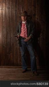 classically dressed middle aged cowboy stands with a revolver in a dark room with wooden walls. middle aged cowboy