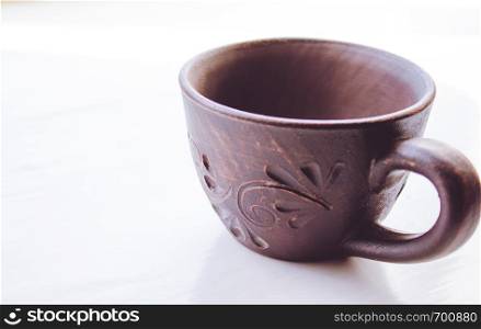 Clay cup stands on a white background. Close-up.. Clay cup stands on a white background.