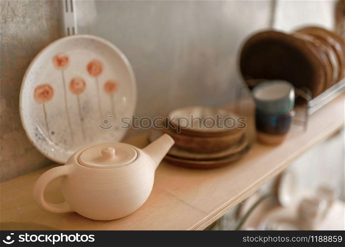 Clay dishware on shelf in pottery workshop, nobody. Handmade tableware molding and shaping, traditional hobby, utensils making