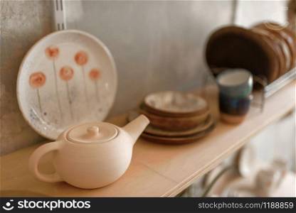 Clay dishware on shelf in pottery workshop, nobody. Handmade tableware molding and shaping, traditional hobby, utensils making