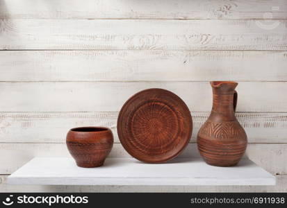 clay jug and plate at shelf on white wooden plank background