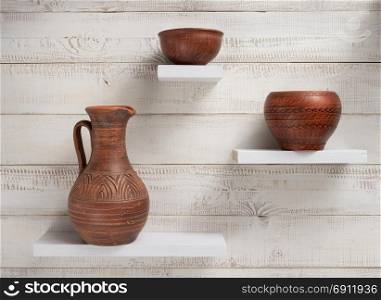 clay jug and plate at shelves on white wooden plank background