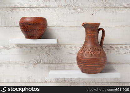 clay jug and pot at shelves on white wooden plank background