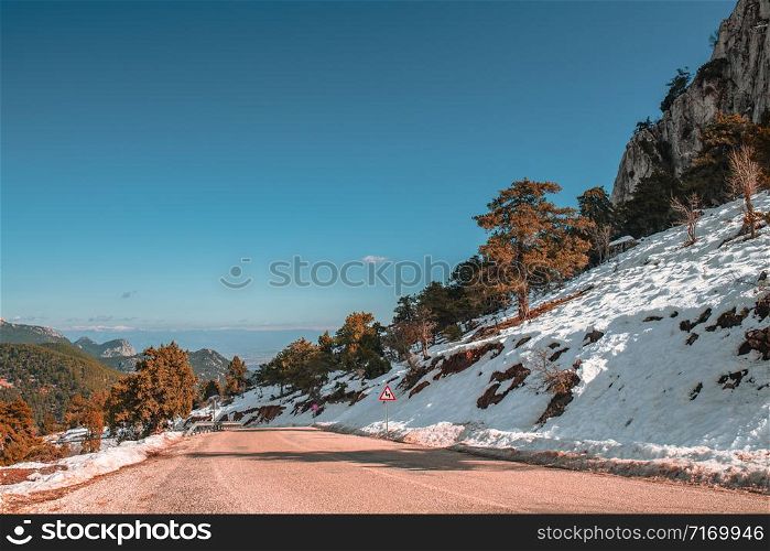 Clean asphalt road with snow on each side in the mountain on clear winter day. Sunny winter day