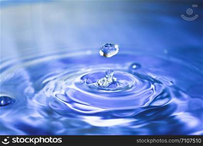 Clean blue drop of water splashing in clear water. Abstract blue background