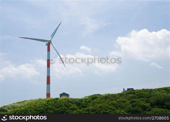 clean energy concept. wind turbine in green hill under cloudy blue sky.