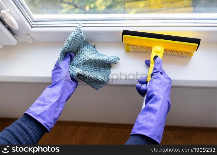 Cleaning and cleaning concept. A young girl in purple gloves holds a rag and a mop for cleaning windows. Cleaning and cleaning concept. A young girl in purple gloves holds a rag and a mop for cleaning windows.
