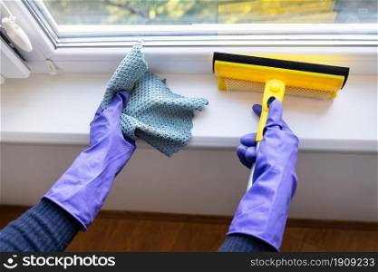 Cleaning and cleaning concept. A young girl in purple gloves holds a rag and a mop for cleaning windows. Cleaning and cleaning concept. A young girl in purple gloves holds a rag and a mop for cleaning windows.