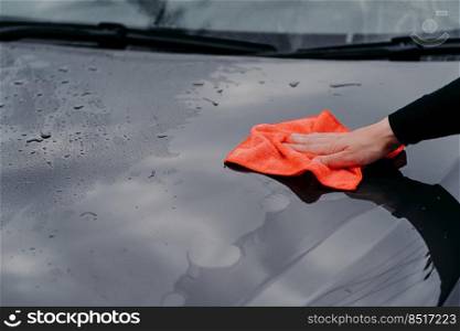 Cleaning car using microfiber cloth. Man washes black auto hood. Polishing vehicle. Car detailing, maintenance