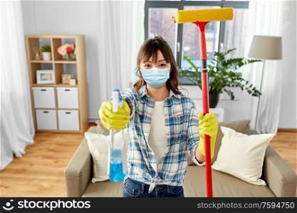cleaning, health and hygiene concept - asian woman wearing protective medical mask for protection from virus in gloves with window cleaner and sponge mop at home. asian woman in protective mask cleaning home