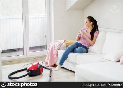 cleaning, household and people concept - happy woman or housewife with vacuum cleaner on floor drinking coffee at home. woman with vacuum cleaner drinking coffee at home. woman with vacuum cleaner drinking coffee at home