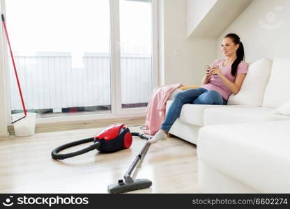 cleaning, household and people concept - happy woman or housewife with vacuum cleaner on floor drinking coffee at home. woman with vacuum cleaner drinking coffee at home