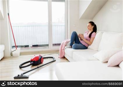 cleaning, household and people concept - happy woman or housewife with vacuum cleaner on floor drinking coffee at home. woman with vacuum cleaner drinking coffee at home. woman with vacuum cleaner drinking coffee at home