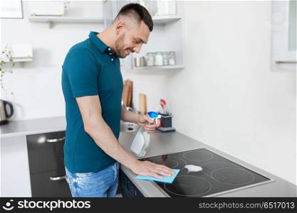 cleaning, household and people concept - man with spray cleaner and cloth wiping cooker at home kitchen. man with rag cleaning cooker at home kitchen. man with rag cleaning cooker at home kitchen