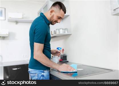 cleaning, household and people concept - man with spray cleaner and cloth wiping cooker at home kitchen. man with rag cleaning cooker at home kitchen. man with rag cleaning cooker at home kitchen
